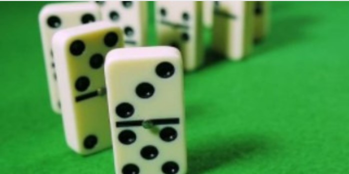 Close-up of white dominoes with black dots standing on green felt surface, shallow depth of field, focused mood